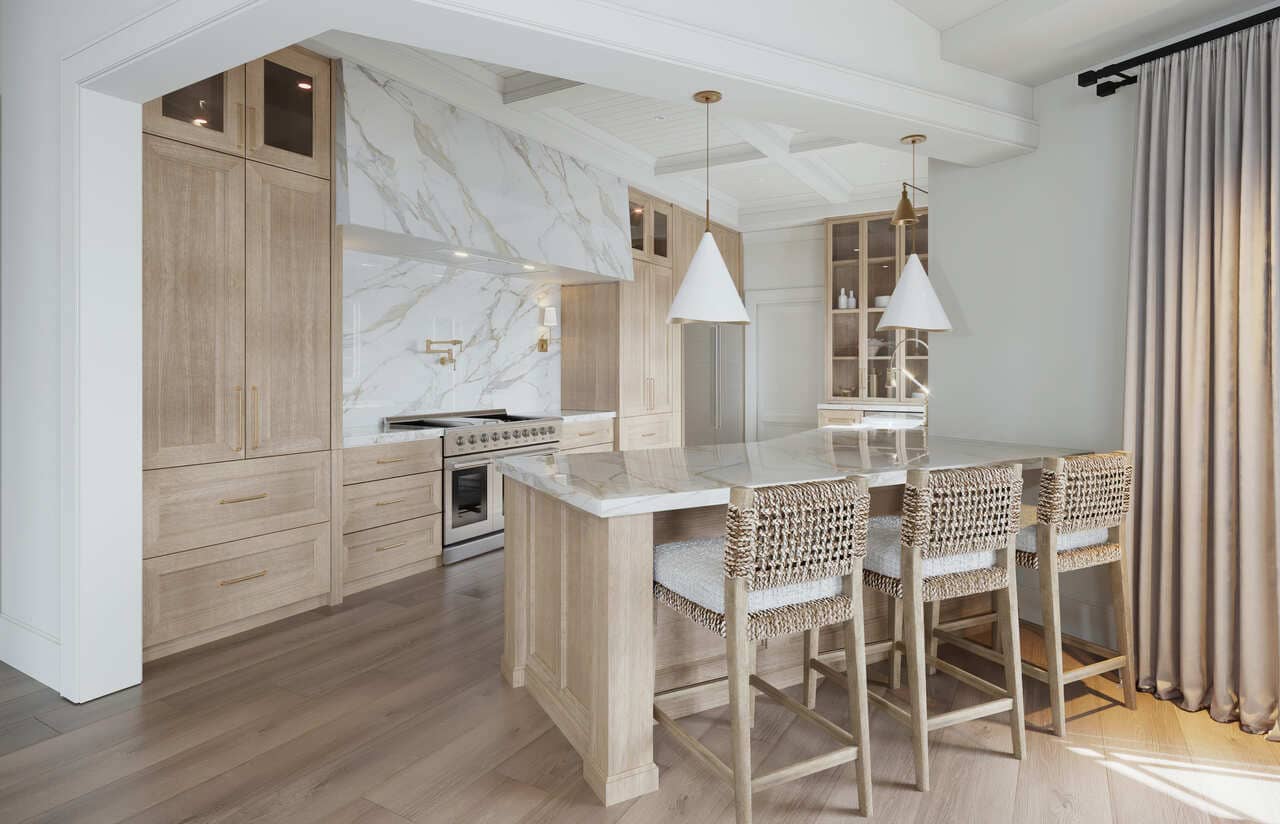 Light oak cabinetry with simple shaker fronts wraps the range wall, while a thick-mitered stone hood and full-height slab backsplash