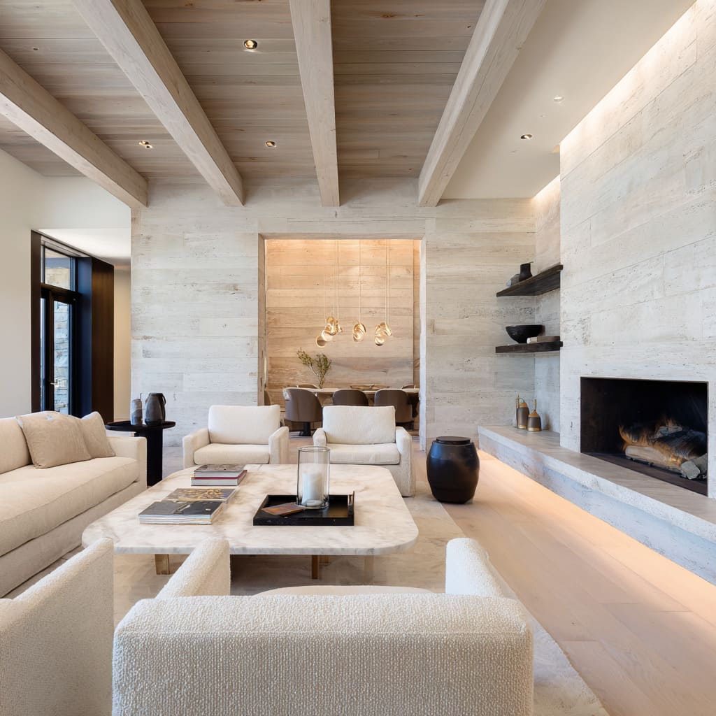 Light-toned modern chalet gathering room styling with bleached driftwood ceiling, creamy stone hearth, ivory boucle furniture, rounded brass table Light-toned modern chalet gathering room styling with bleached driftwood ceiling, creamy stone hearth, ivory boucle furniture, rounded brass table