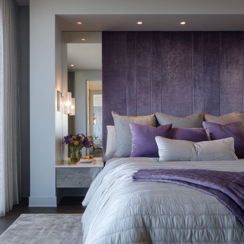 Dormitorio en violeta profundo y plata con cabecero alto de terciopelo, paneles laterales espejados y apliques de cristal. Dormitorio en violeta profundo y plata con cabecero alto de terciopelo, paneles laterales espejados y apliques de cristal.