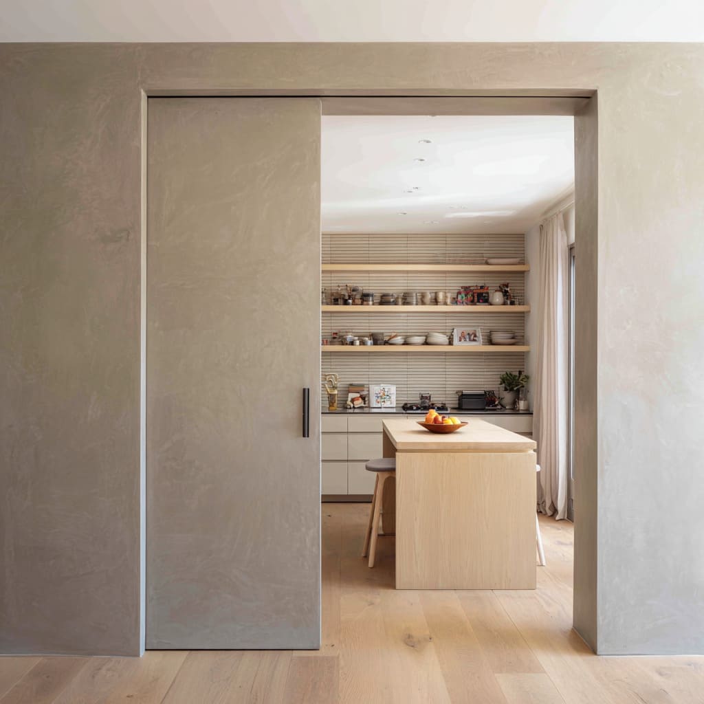 Concept with a greige microcement pocket door revealing a graphic kitchen with slatted backsplash and wood island