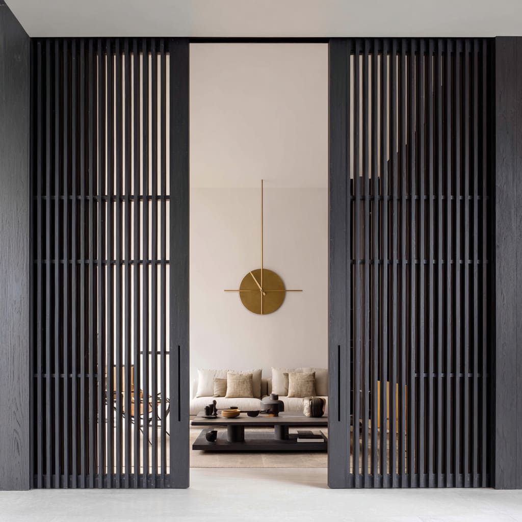 Dark slatted pocket doors ideas framing a sculptural lounge with pale seating and a gold clock Dark slatted pocket doors ideas framing a sculptural lounge with pale seating and a gold clock