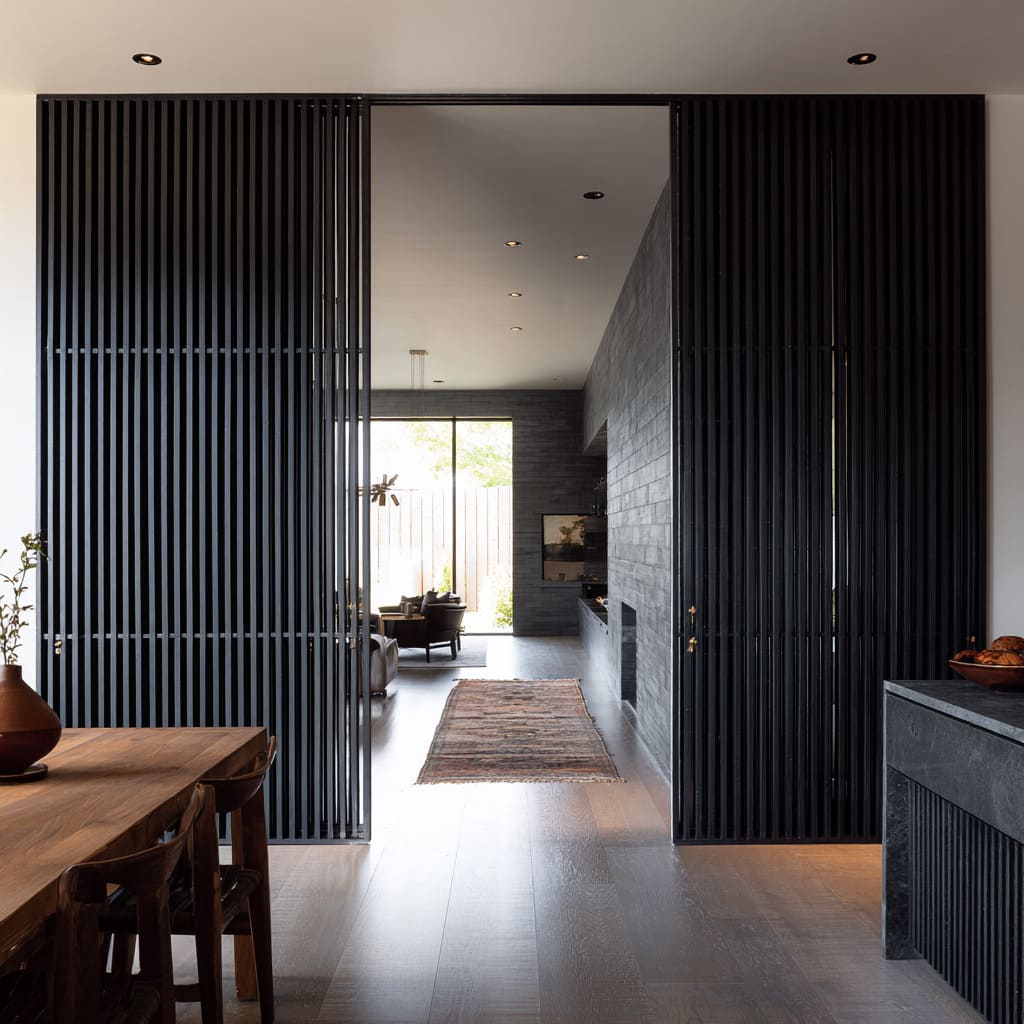 Large slatted sliding doors ideas forming a continuous ribbed wall that opens to a lounge with brick and wood textures
