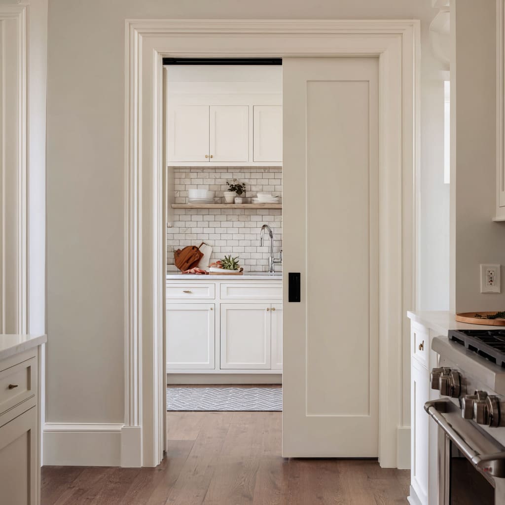 White paneled pocket door design joining a bright utility kitchen with a warm, classic cooking space White paneled pocket door design joining a bright utility kitchen with a warm, classic cooking space